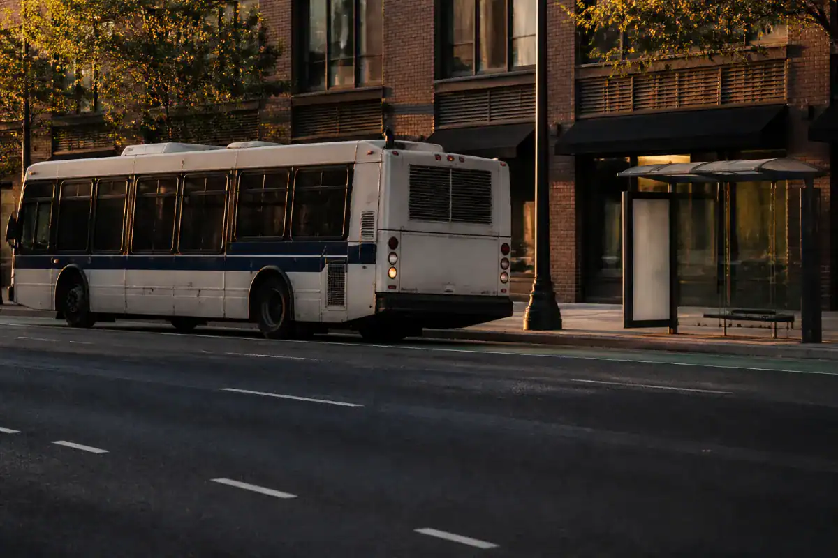 A New York city bus pulling away from a stop alongside a painted bicycle lane, seen from across the street in late afternoon, empty lane in the foreground