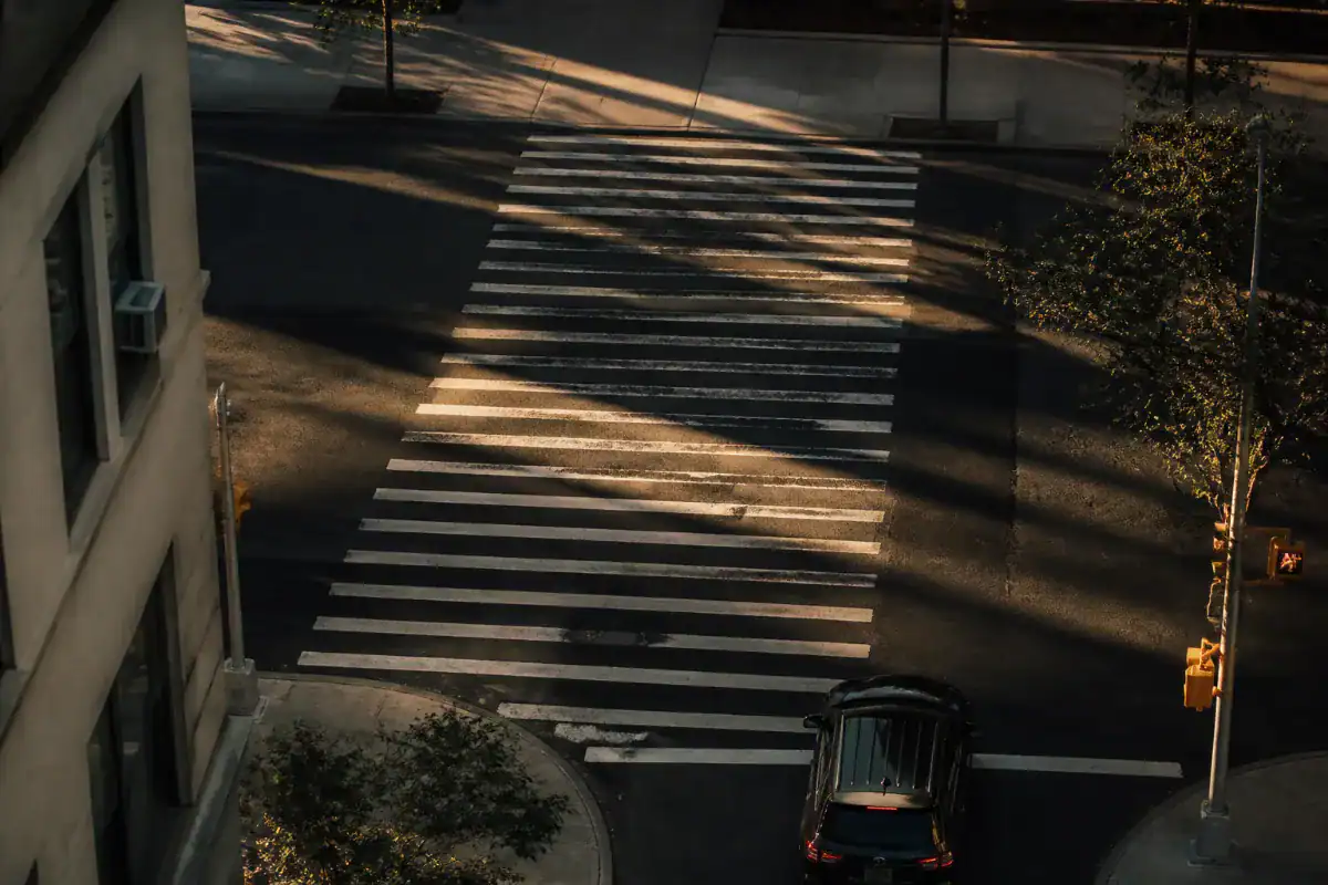 An empty marked pedestrian crossing photographed from an upper window in late afternoon, long shadows across the white stripes, one car waiting at the line