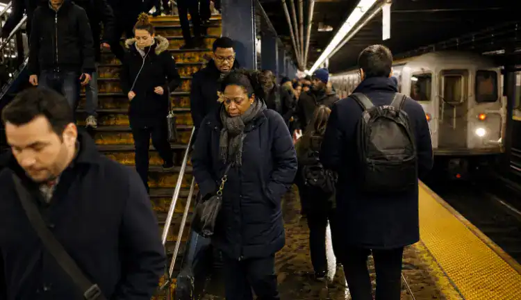 Crowded Brooklyn subway platform at rush hour, commuters in coats on a damp stairway as a train arrives.