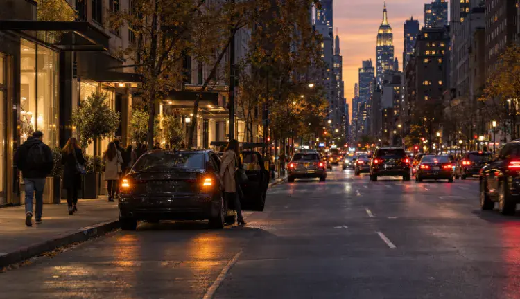 A dark sedan pulled over on a Manhattan avenue at night as a passenger steps out onto the sidewalk.